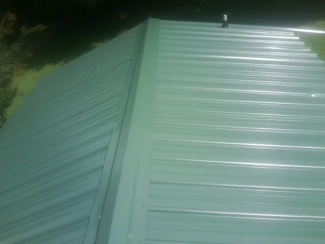 New green metal panels meeting at the ridge of a roof — Flat Roof Repair work by our crew in Alexander